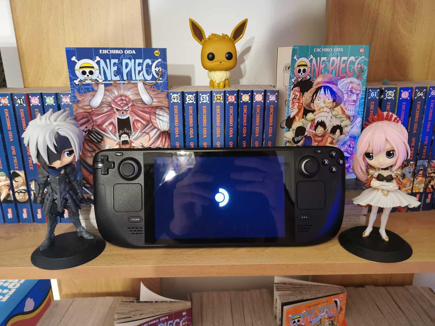 Das Steam Deck auf einem Regal neben kleinen Figuren und der Manga-Reihe "One Piece" im Hintergrund