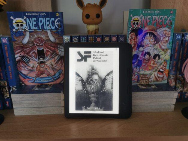 Cover von "Picknick am Wegesrand" vor einem Regal mit One Piece Bänden